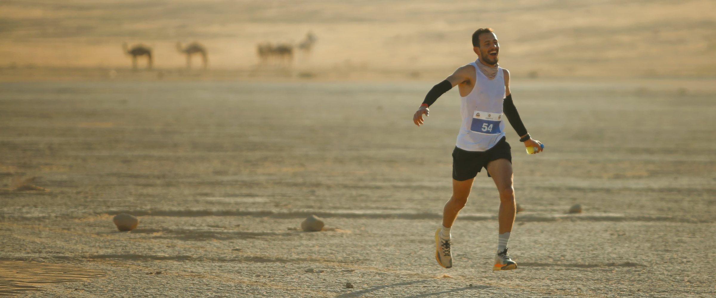 Fuad Abu Safi running across the desert floor at Wadi Rum, with camels grazing in the distance